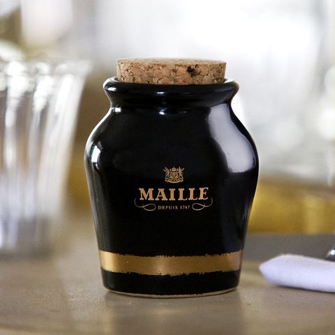 Black Maille mustard jar with gold crest and cork lid on a restaurant table