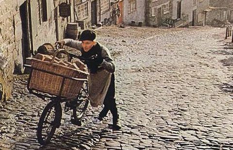 Man pushing bicycle with large basket up hill on a cobble stone road