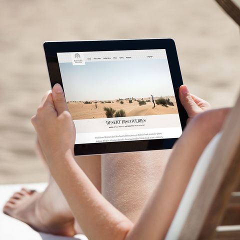 Reader on a sun lounger holding a tablet showing the Raffles magazine article Desert Discoveries